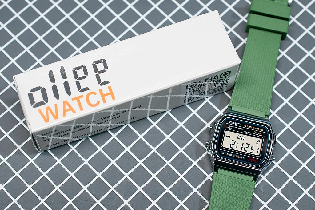 Ollee Watch retail box next to a Casio A158 fitted with the mod and a green rubber strap