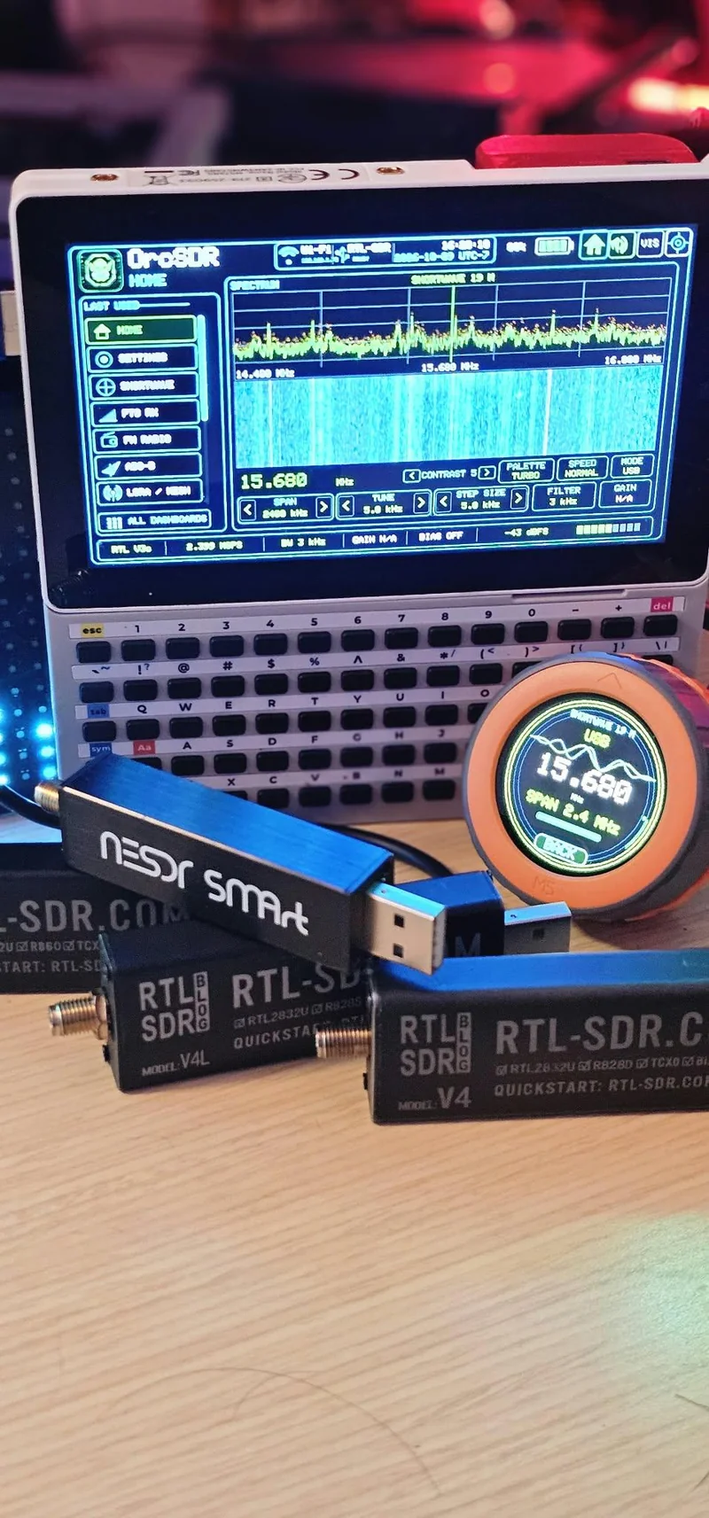 M5Stack Tab5 in a keyboard clamshell running OrcSDR shortwave at 15.680 MHz USB with M5Dial showing the same frequency plus NESDR SMArt and RTL-SDR Blog V4 dongles